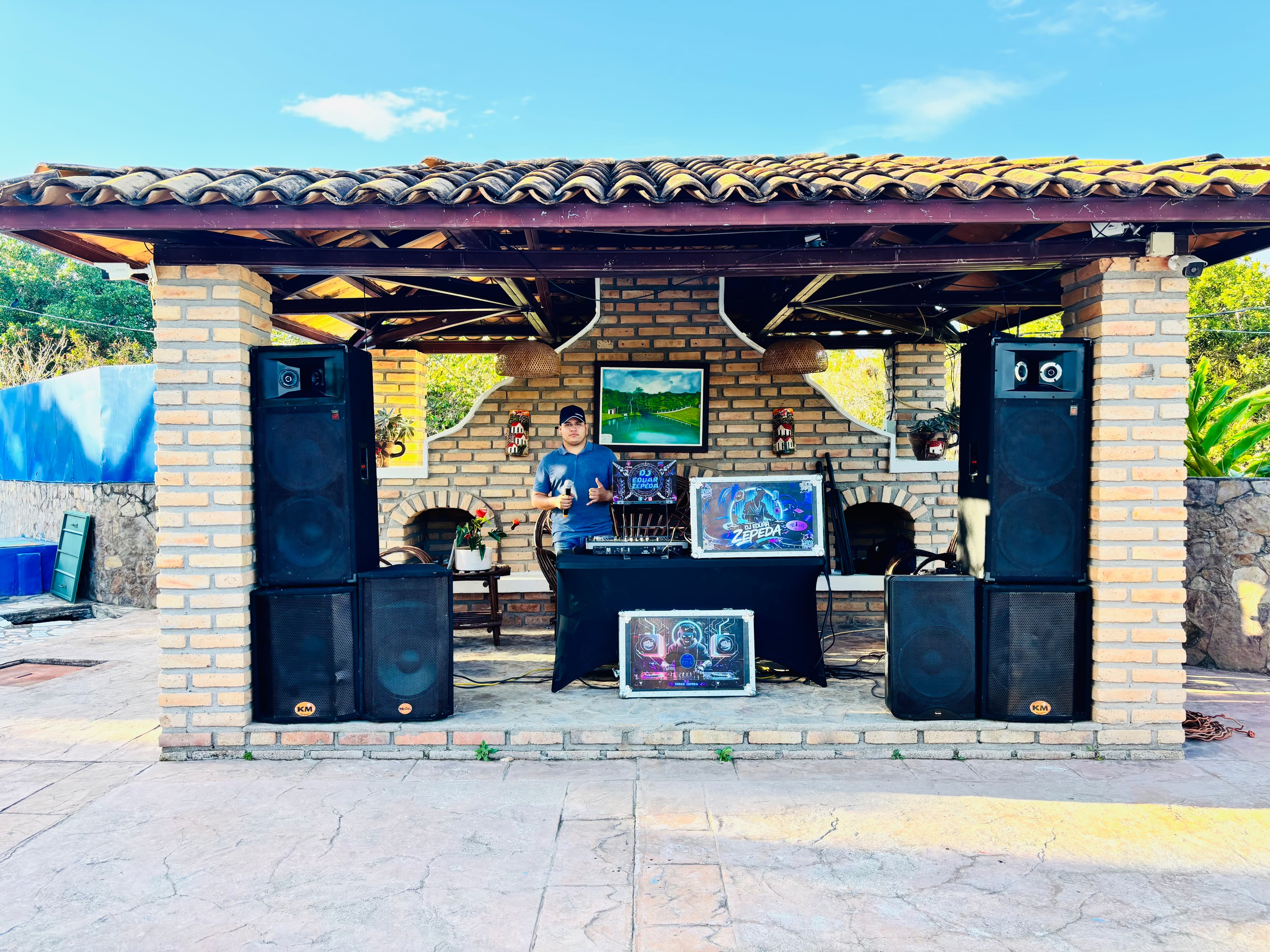 DJ Eduar Zepeda posa con su equipo de sonido en un pabellón rústico de ladrillo.