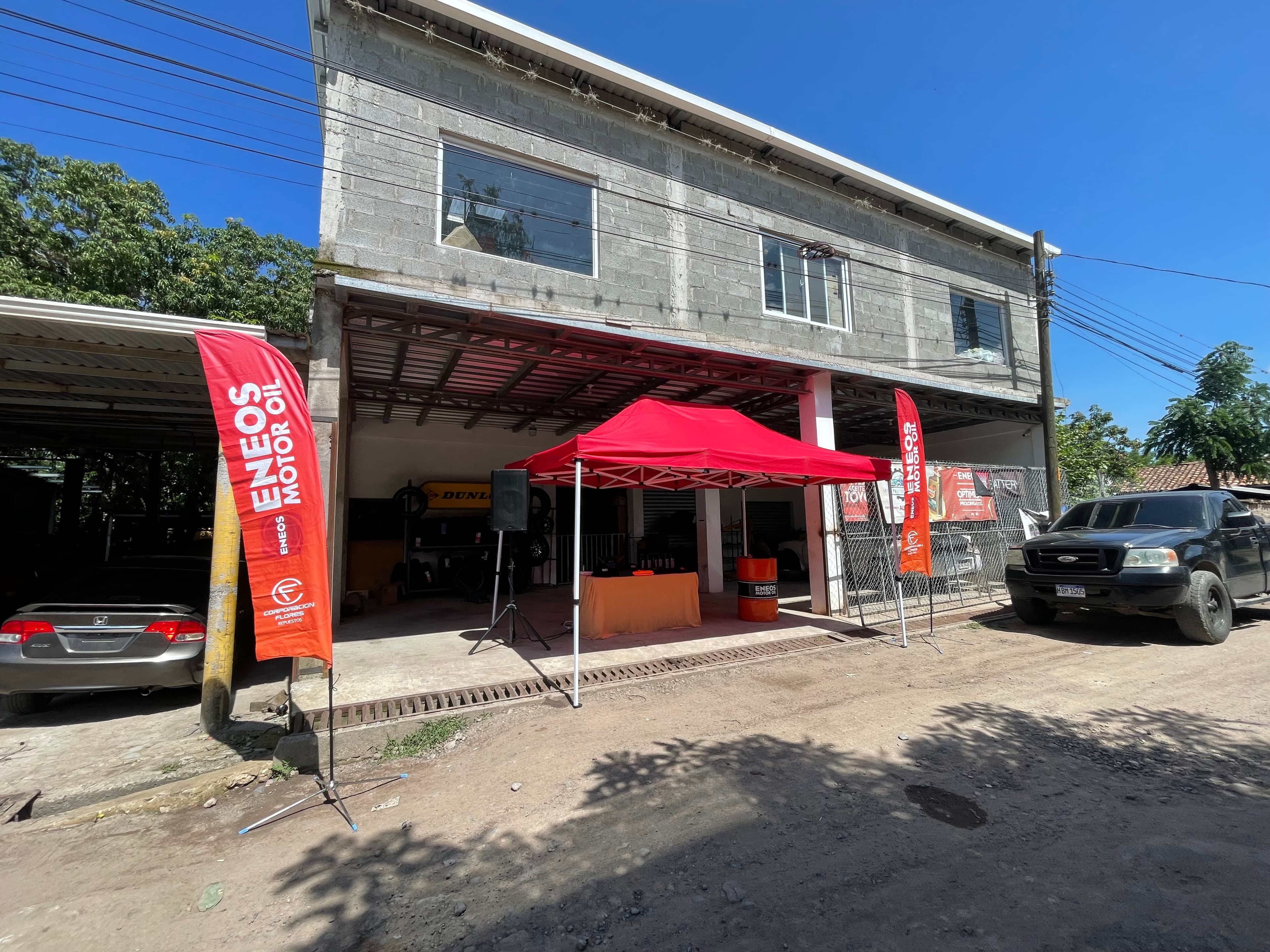 Carpa roja y banderas de Eneos Motor Oil frente a un edificio gris con vehículos.