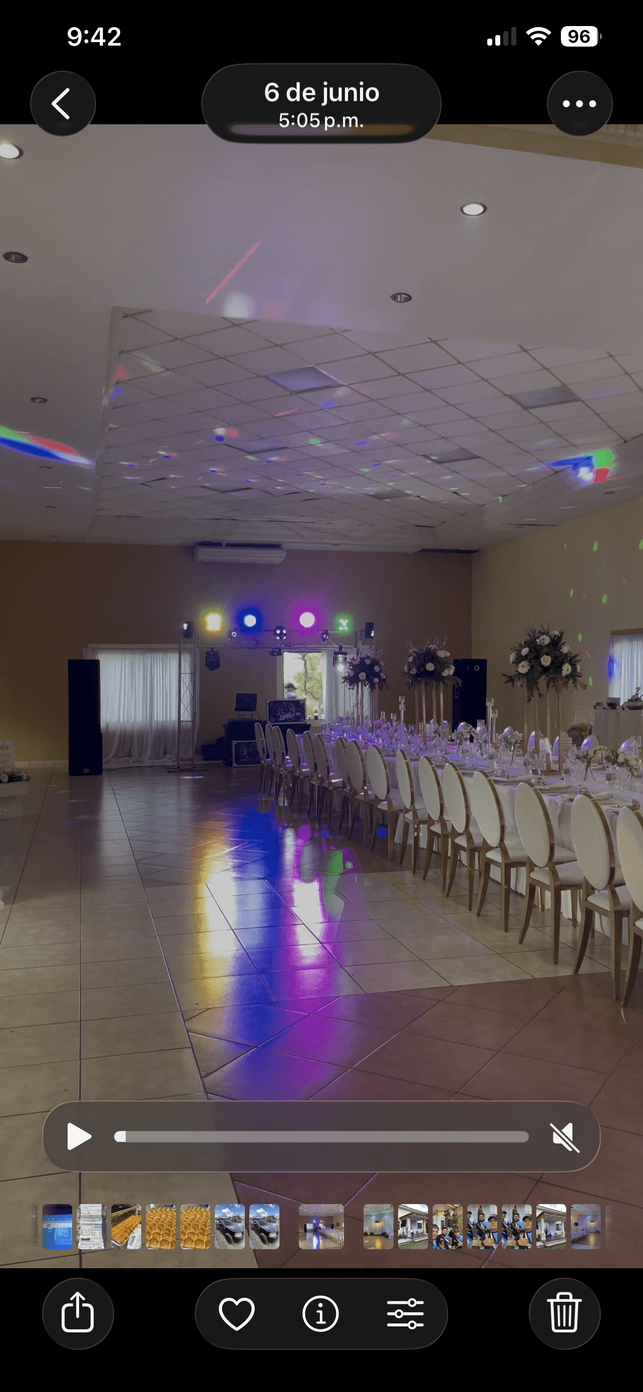 Salón de eventos con mesa larga, sillas blancas y luces de colores reflejadas.